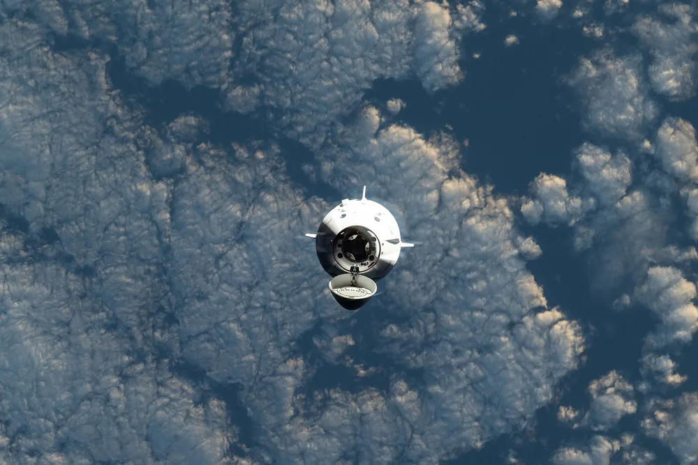 A SpaceX Dragon capsule approaches the space station high above white clouds over the Indian Ocean