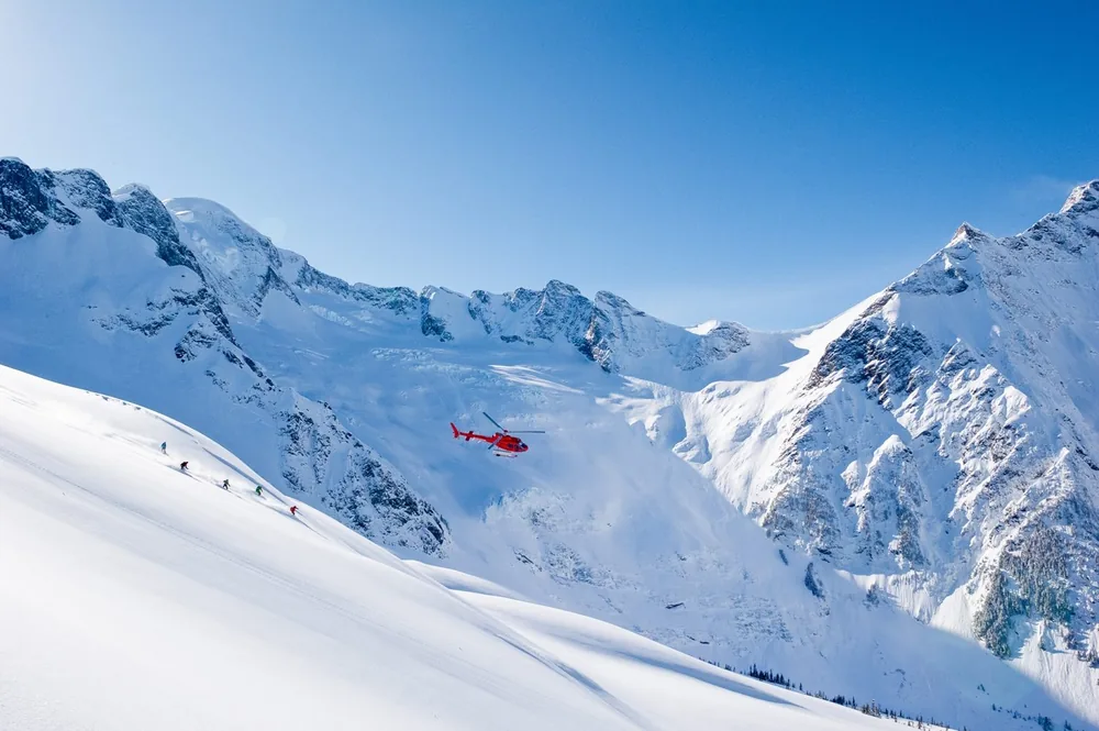 A helicopter flies above snow-covered peaks in the Coast Mountains of British Columbia