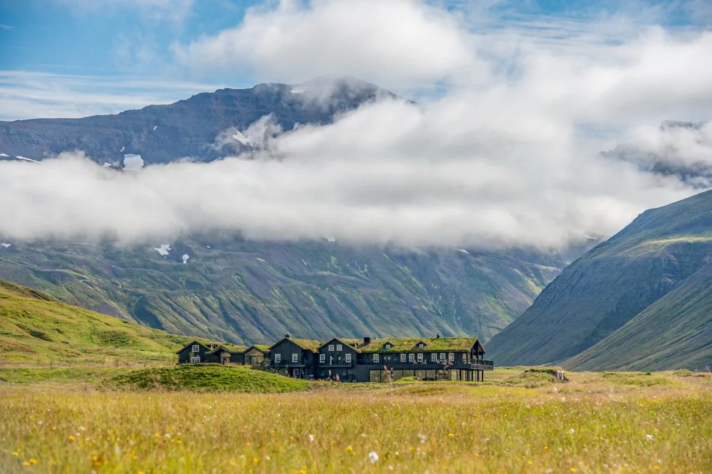 A low turf-roofed lodge in a green Icelandic valley beneath clouded mountains