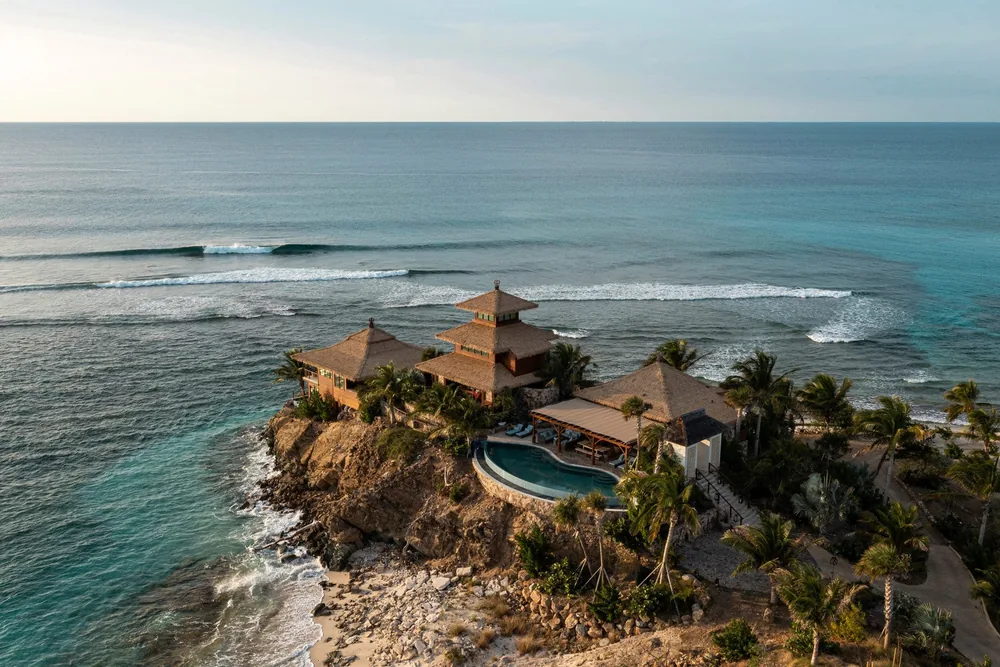 Thatched clifftop houses and an infinity pool above the sea at sunset on Necker Island