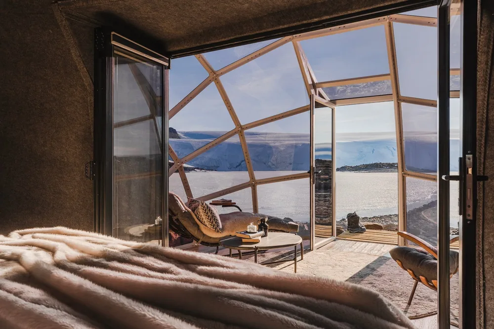A warm sleeping pod with a sheepskin-draped bed and a curved glass wall looking out over Antarctic ice